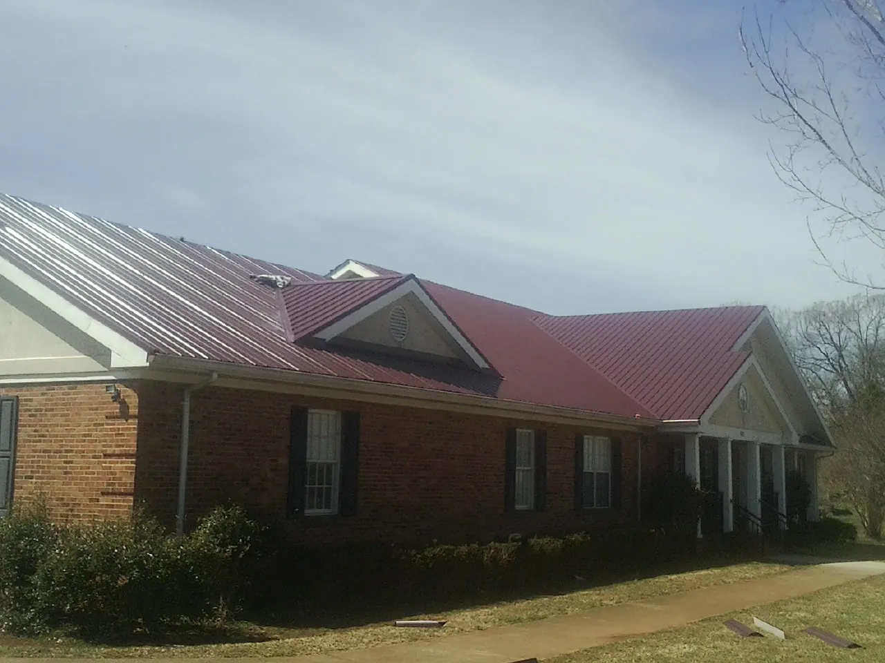 Red metal roof with gabled entries on a long brick building, from a Hail Damage Roof Repair job in Pilot Mountain