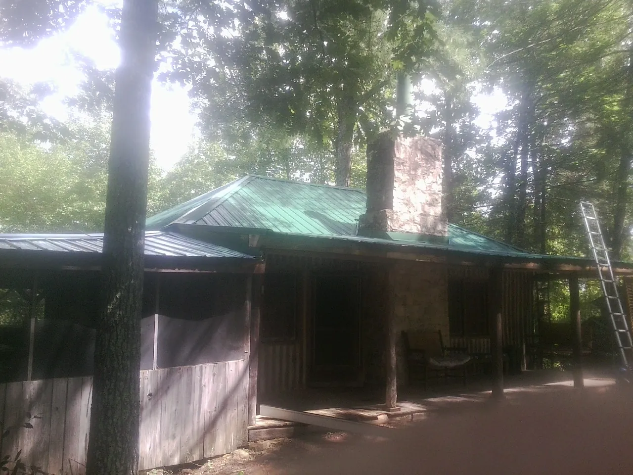 Green metal roof and stone chimney above a log cabin porch in Pilot Mountain