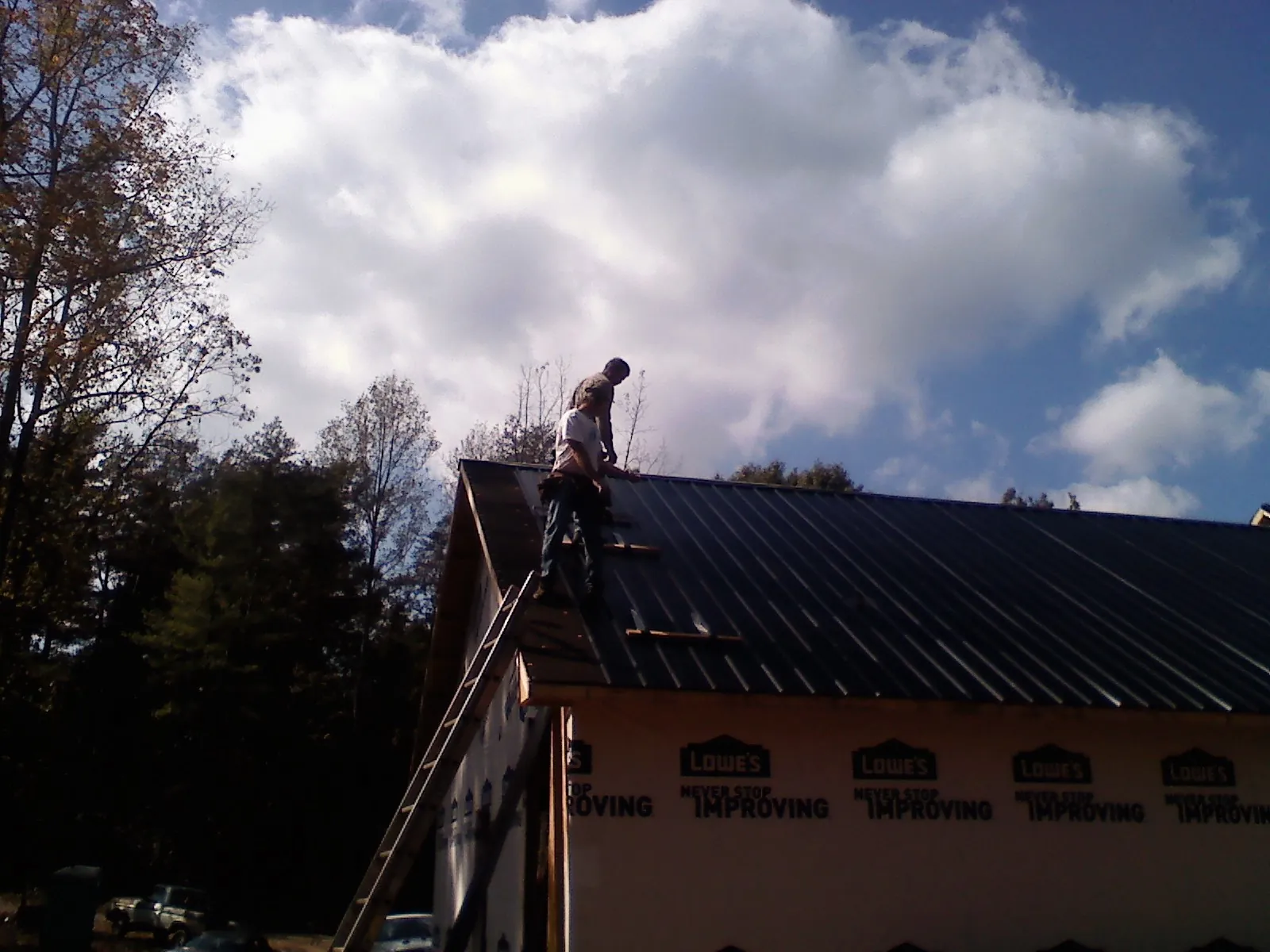 Roofer fastening dark metal panels high against a cloudy sky, from a Roof Inspection job in Pilot Mountain