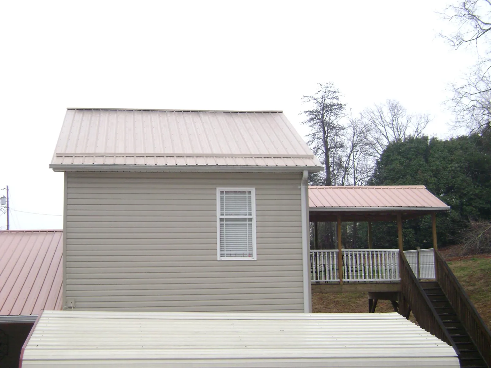 Tan metal roofs on a two story addition and attached porch, from a Roof Replacement job in Pilot Mountain